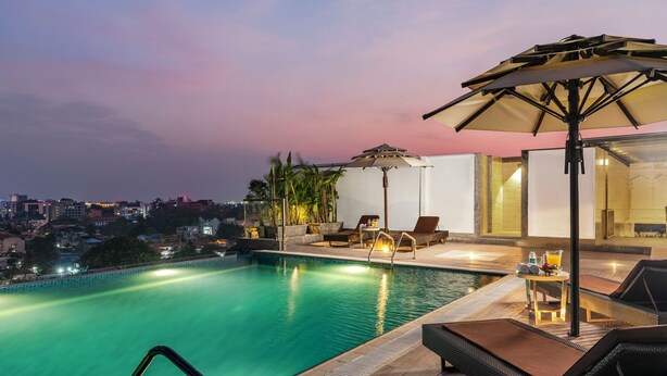 Una piscina a sfioro sul tetto con lettini prendisole e un ombrellone, con vista sulla città al crepuscolo.