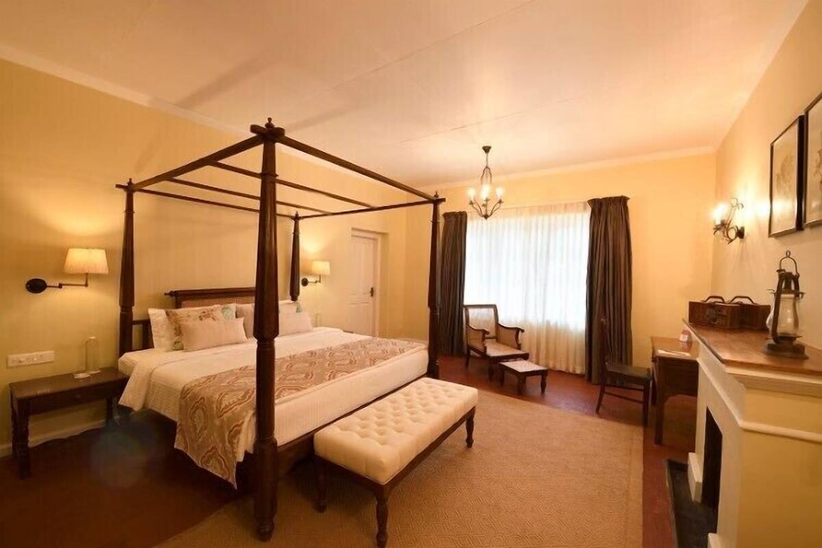 A four-poster bed, a bench, a desk, and a chair in a hotel room.