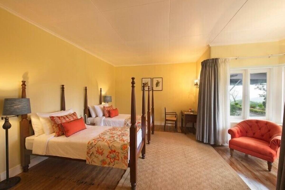 A bedroom with a four-poster bed, a chair, a small table, and a window with curtains.