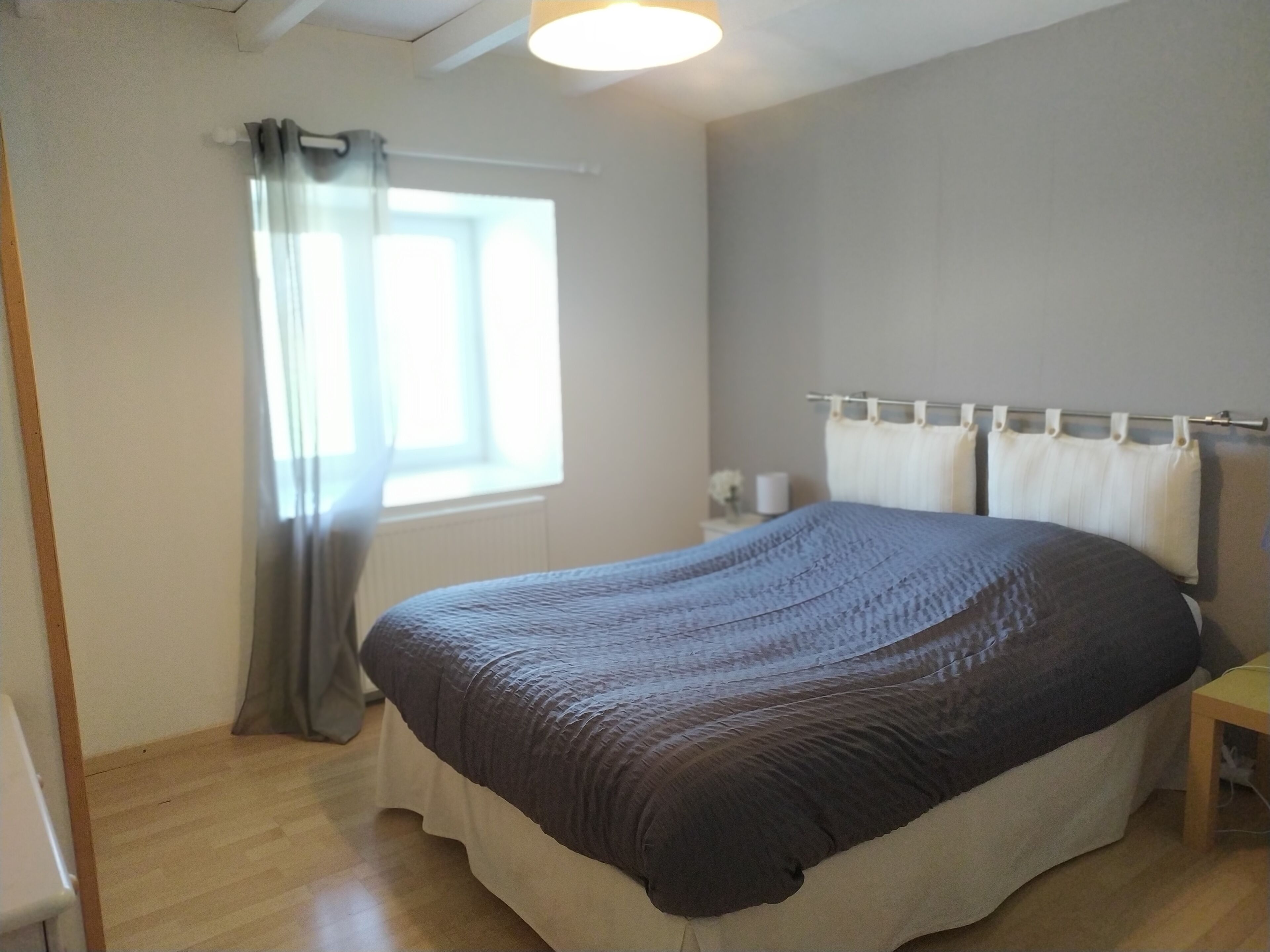 Un dormitorio con cama, ventana con cortinas, mesita de noche y velador.