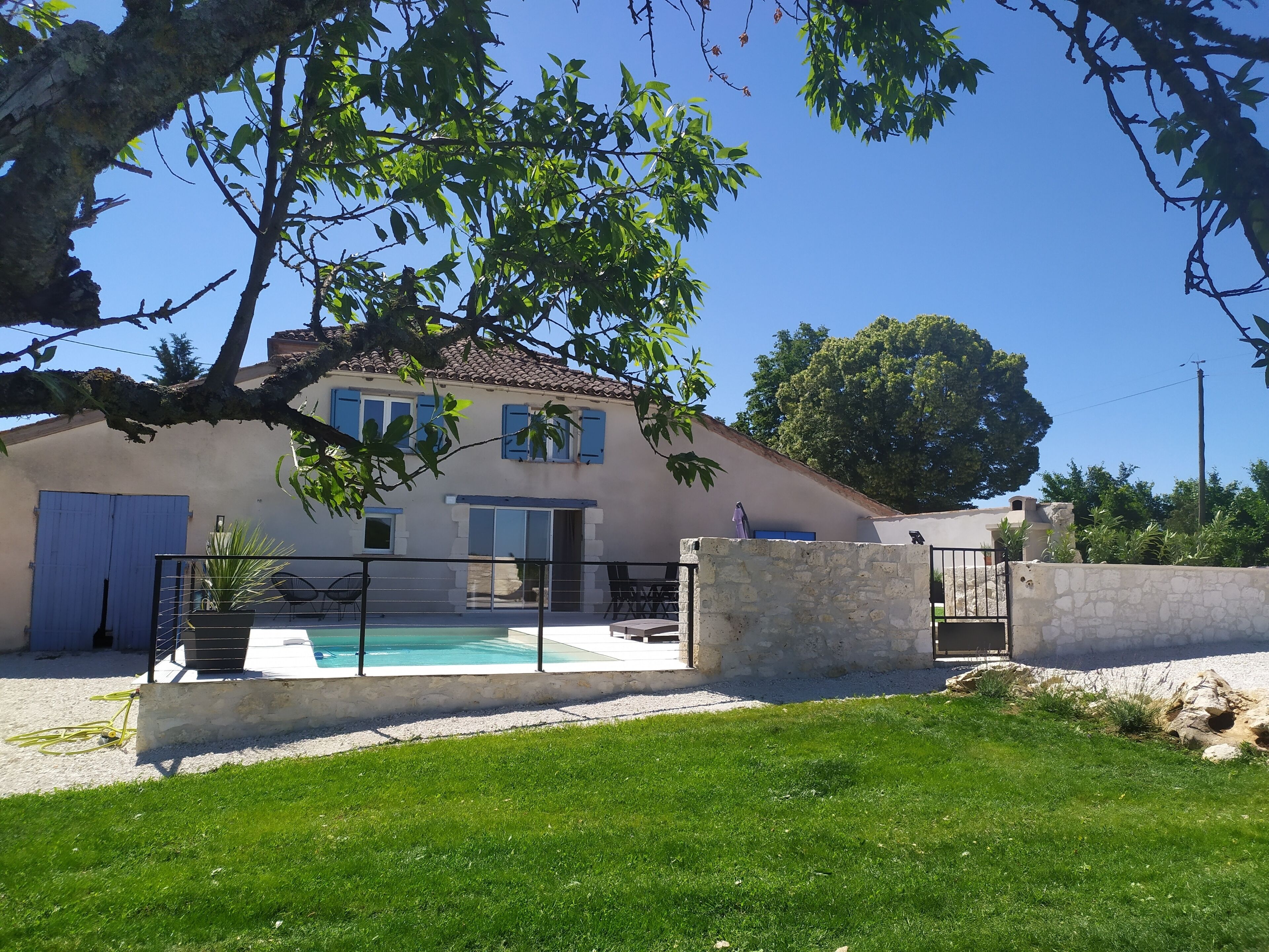 A house with a swimming pool, surrounded by a stone wall and a grassy lawn.