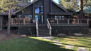 Une cabane à deux étages dotée d’un balcon, d’un escalier menant à une terrasse, et entourée d’une zone boisée.