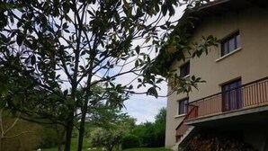 Een gebouw met een balkon, een boom op de voorgrond en een gazon.