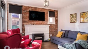Ein Wohnzimmer mit Kamin aus Backsteinen, einem Flachbildfernseher, roten und grauen Sofas und zwei gerahmten Kunstwerken an der Wand.