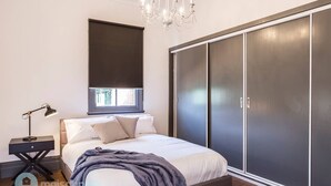Ein Schlafzimmer mit einem Bett, einem Nachttisch, einer Schreibtischlampe, einem großen Kleiderschrank und einer Chandelier.