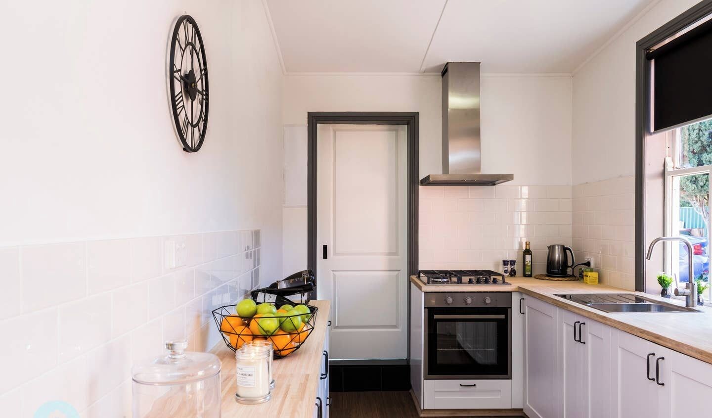 A narrow kitchen with white cabinets, a gas stove, a stainless steel range hood, and a window with a view of the outside.