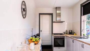 A narrow kitchen with white cabinets, a gas stove, a stainless steel range hood, and a window with a view of the outside.