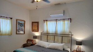 A bedroom with a bed, two bedside tables, a ceiling fan, and two wall-mounted air conditioners. - Room #6 Master with one king size bed, one double bed & one double bunk bed (La Ribera)