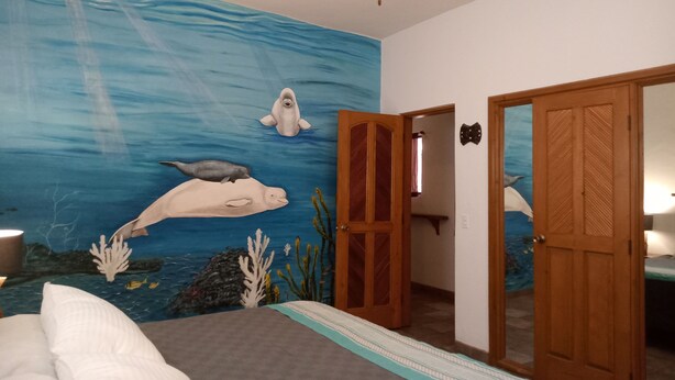 A bedroom with a mural of marine life on the wall, a bed, a ceiling fan, and a wooden door. - Room #6 Master with one king size bed, one double bed & one double bunk bed (La Ribera)