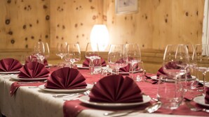 A dining table set with red napkins, plates, and wine glasses, with a wooden wall and a framed picture in the background. - Hotel Gabl by Alpeffect Hotels (Sankt Anton am Arlberg)