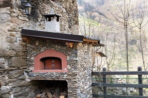 A stone building with a red-tiled fireplace, a wooden beam above it, and a stone wall. - Stone mountain home  (salza di pinerolo)