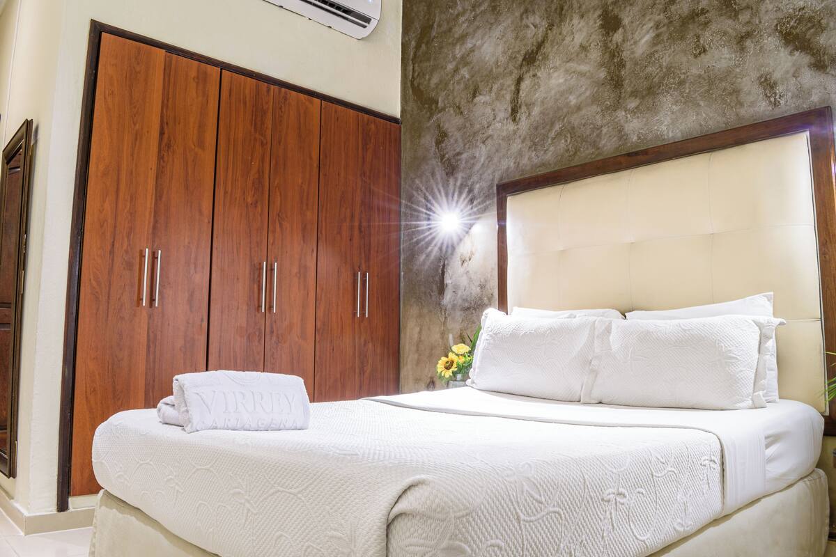 A neatly made bed with white linens and pillows, a wooden wardrobe, and a textured wall.