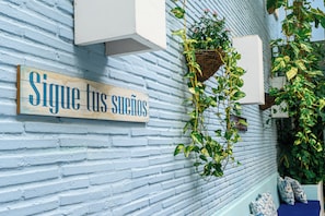 Un muro di mattoni blu con un cartello di legno con la scritta 'Sigue tus sueños' e una pianta sospesa.
