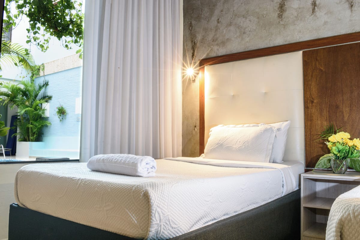 A neatly made bed with a white comforter and a rolled towel, a wooden headboard, and a bedside table with a vase of flowers.