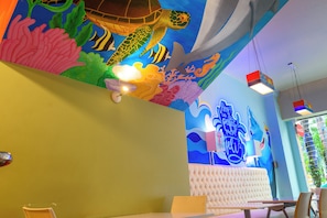 Un ristorante con un murale vivace a tema marino sul soffitto, una zona salotto con sedute imbottite e lampade a sospensione.