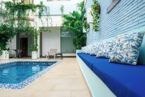 A pool area with a blue and white tiled pool, a blue sofa with floral cushions, and potted plants.