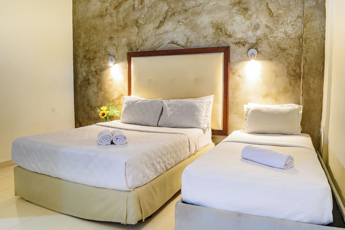 Two beds with white linens, a wooden headboard, and a textured wall behind.