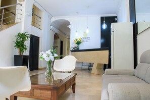 A modern hotel lobby with a reception desk, a sofa, a dining table, and a potted plant. - Hotel Virrey Cartagena (Cartagena)