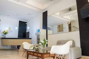 A hotel reception area with a reception desk, two white chairs, a coffee table, and a vase with flowers.