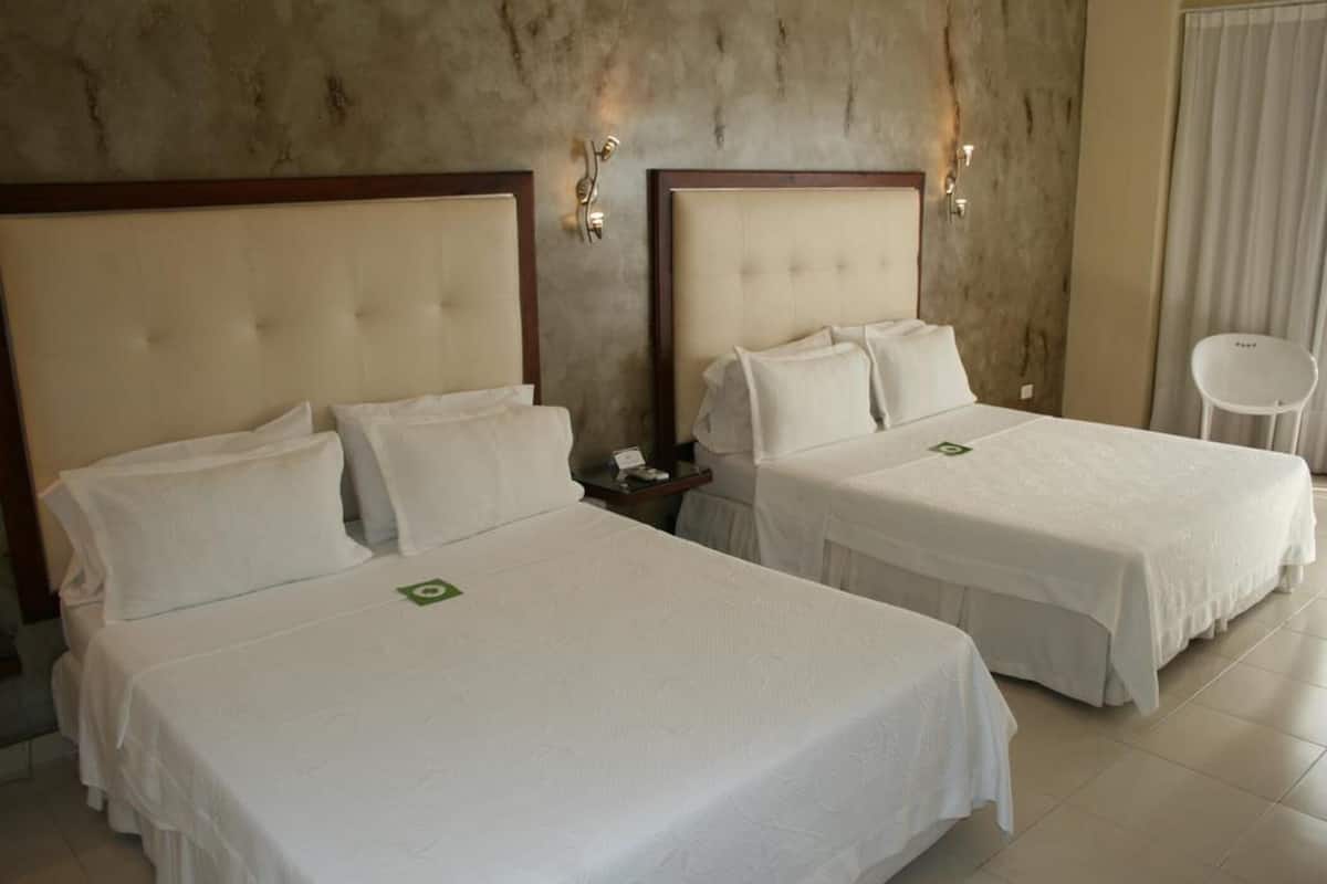 A hotel room with two beds, each with a headboard and white bedding. There are wall-mounted light fixtures and a chair in the corner.