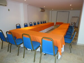 Un salón de conferencias con una larga mesa, sillas azules y un mantel naranja.