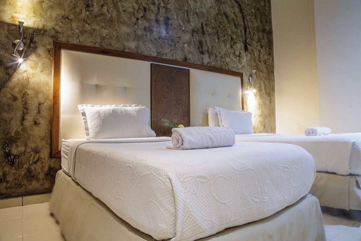 A hotel room with a large bed, a smaller bed, and a marble wall.