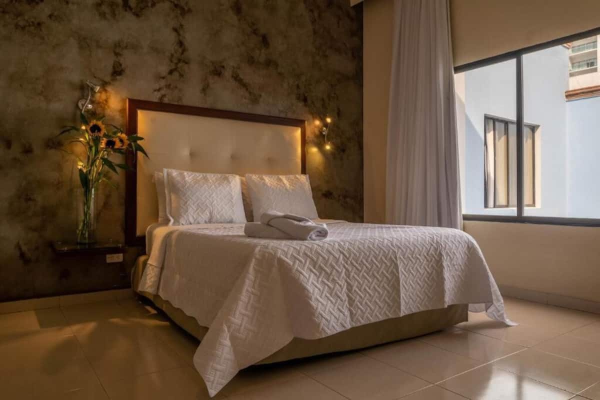 A neatly made bed with a white quilt, a vase with sunflowers, and a wall with a textured pattern.