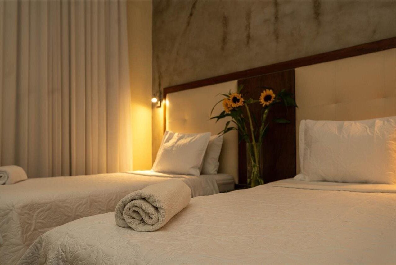 A hotel room with two beds, a large mirror, and a vase with sunflowers.