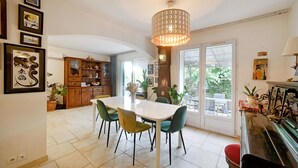 Un vaste espace dédié à la salle à manger, avec une table et des chaises blanches, un buffet en bois doté de portes en verre et une grande horloge murale.