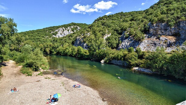 Une rivière aux eaux claires, bordée de collines verdoyantes et de falaises rocheuses.