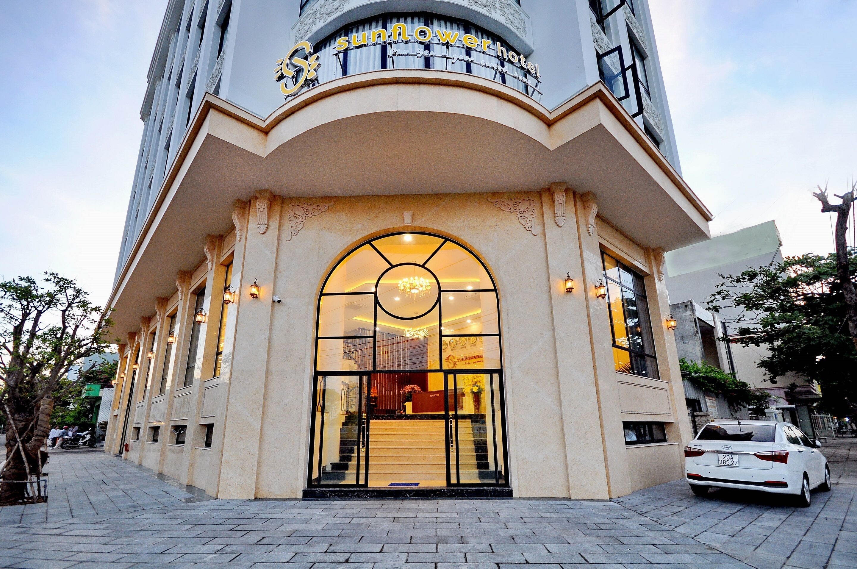 A hotel entrance with a large arched doorway, a reception desk inside, and a car parked outside.