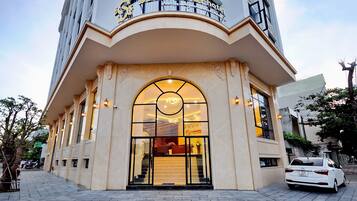 A hotel entrance with a large arched doorway, a reception desk inside, and a car parked outside.