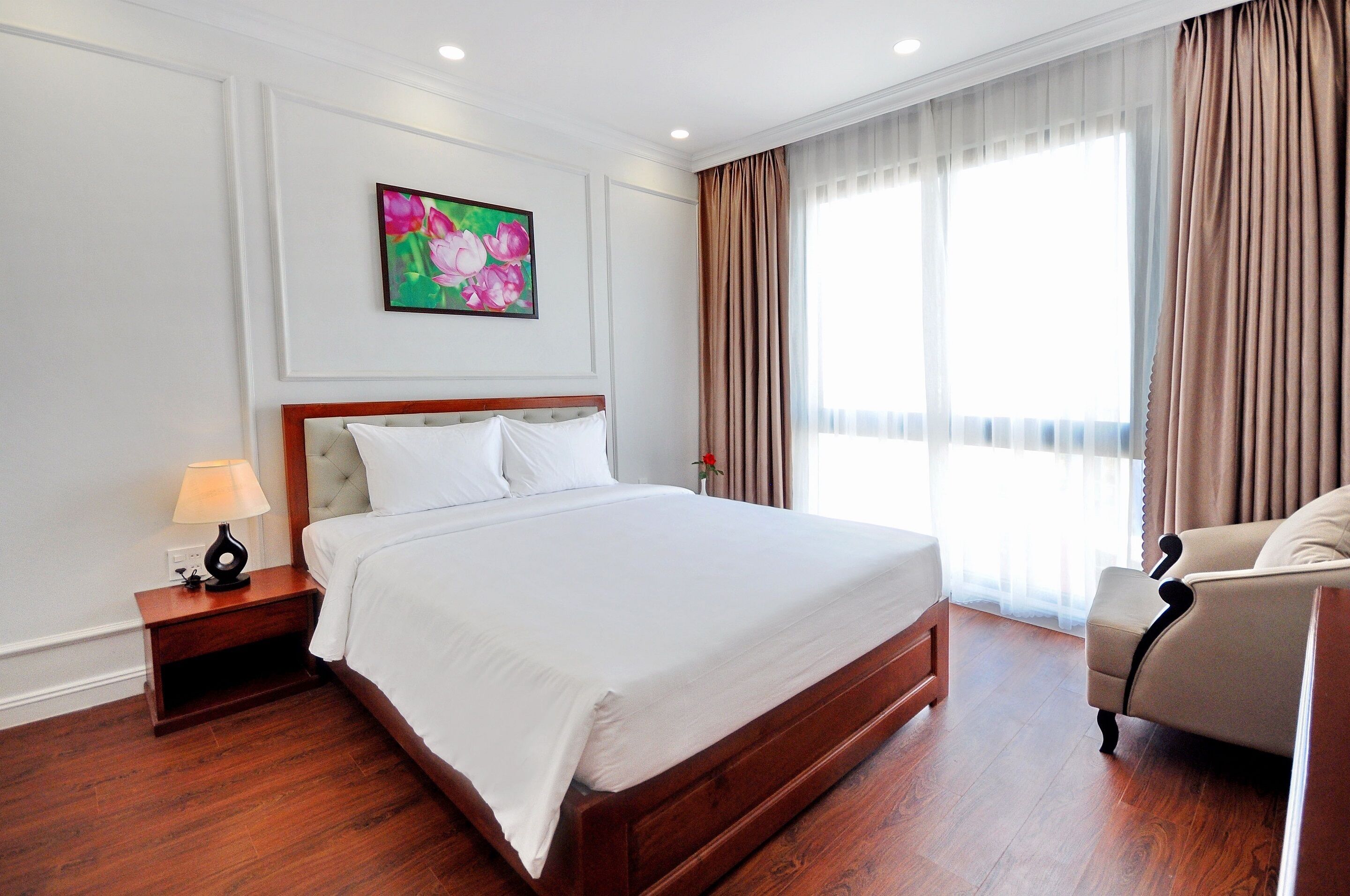 A hotel room with a large bed, a nightstand with a lamp, a chair, and a window with curtains.