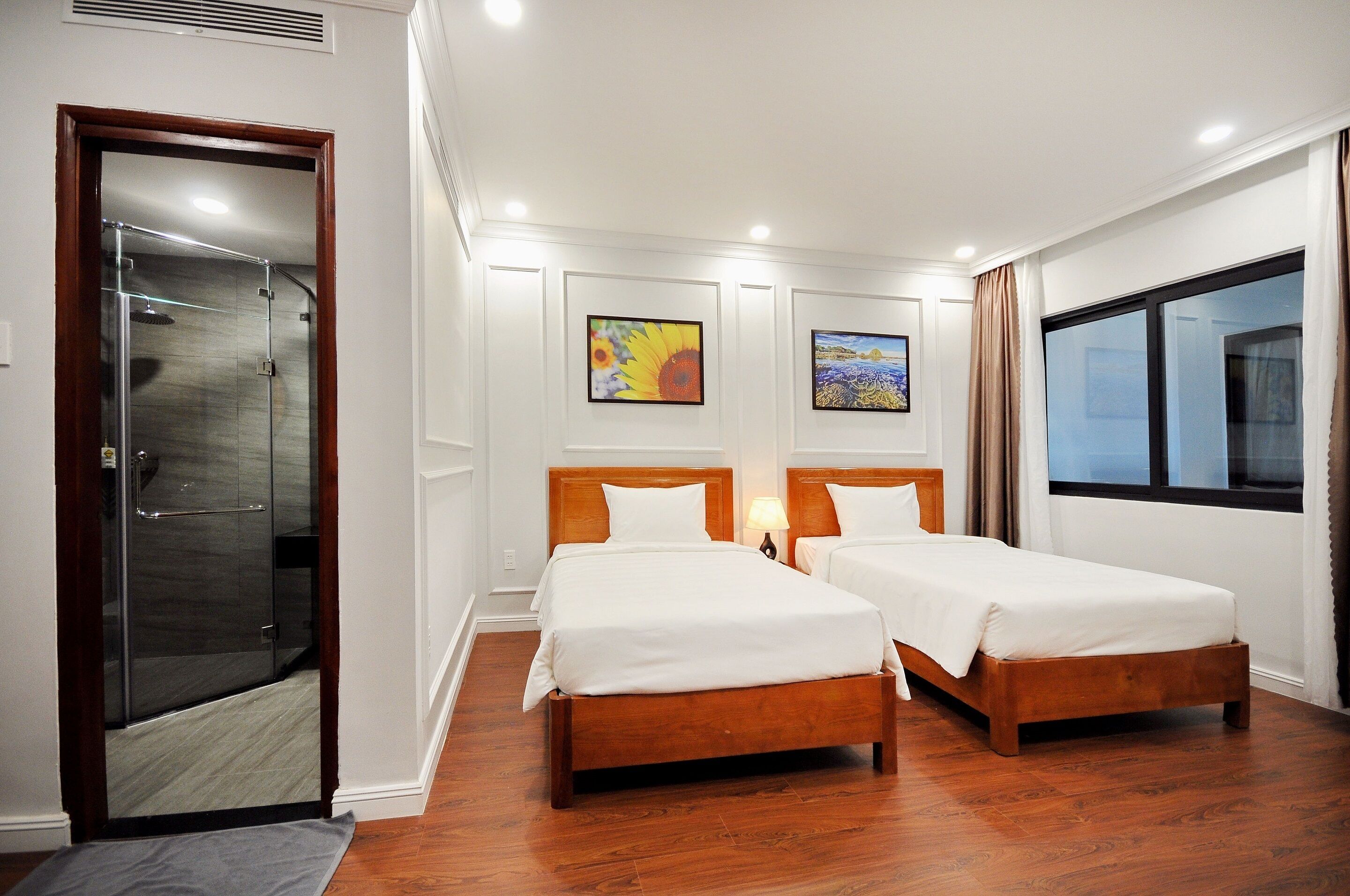 A hotel room with two wooden beds, a glass shower door, and artwork on the walls.