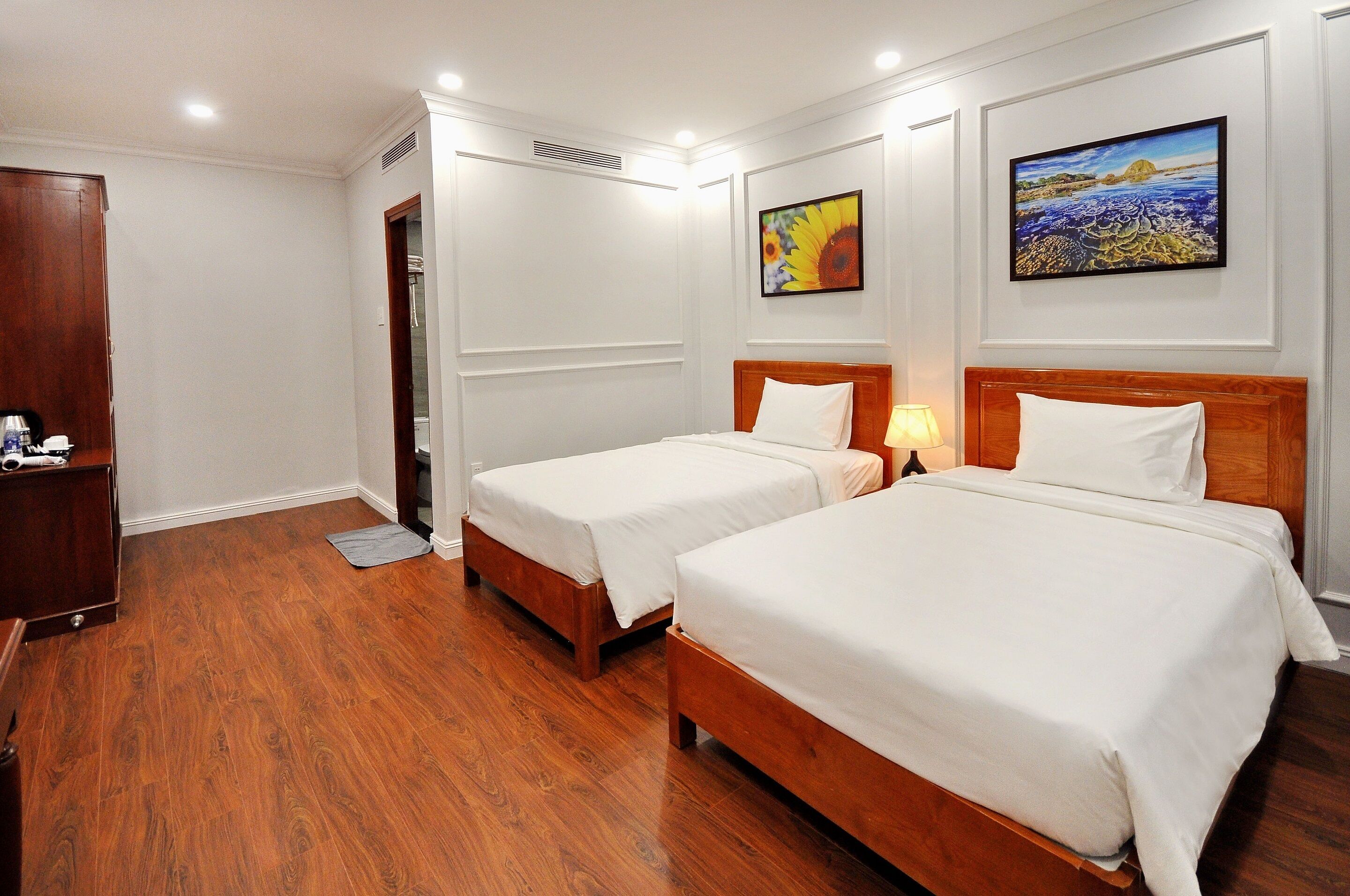 Ein Hotelzimmer mit zwei Betten, Holzboden, weißen Wänden und zwei Bildern.