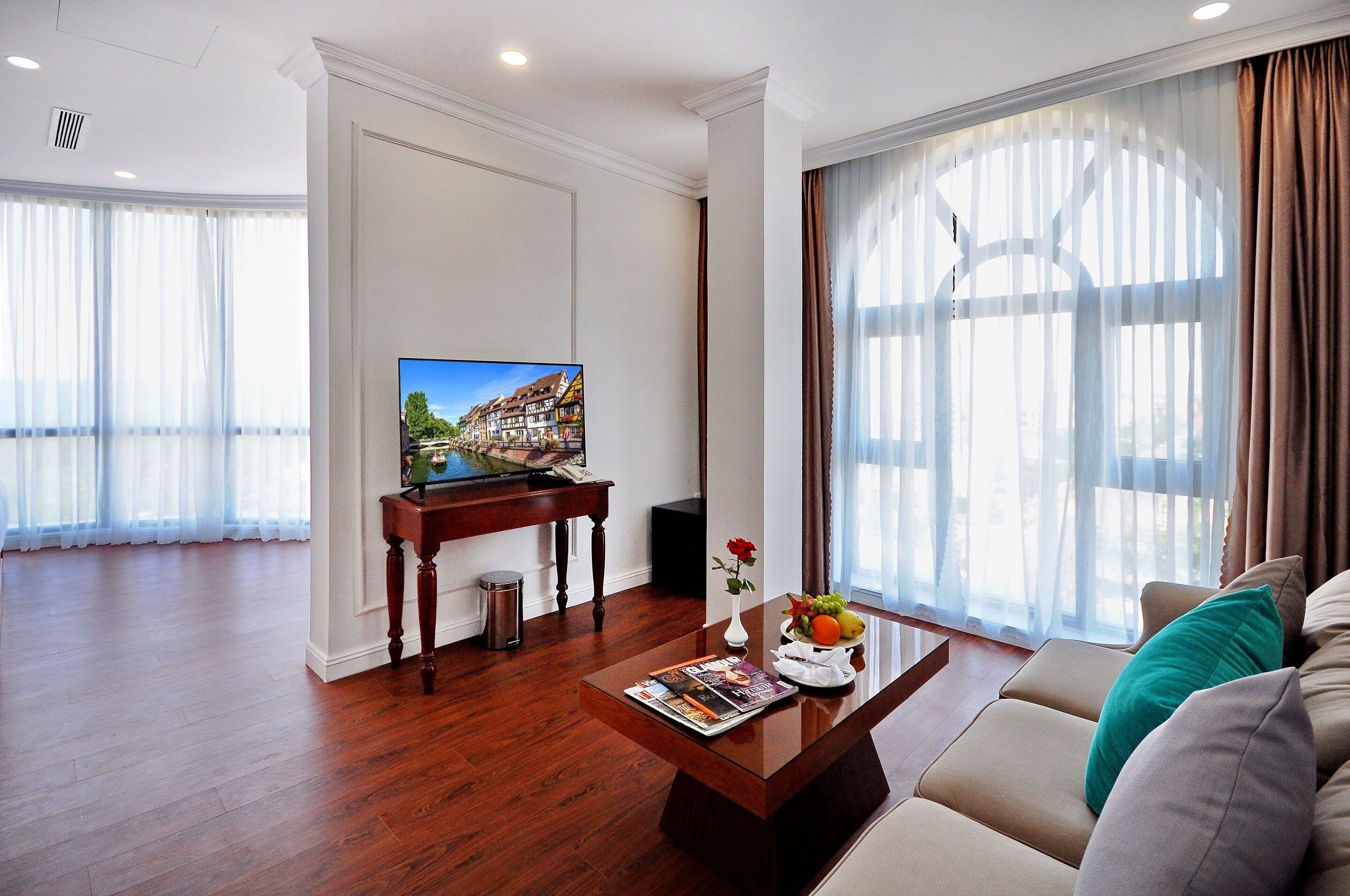 A modern living room with a wooden coffee table, a sofa, a TV, and a window with sheer curtains.