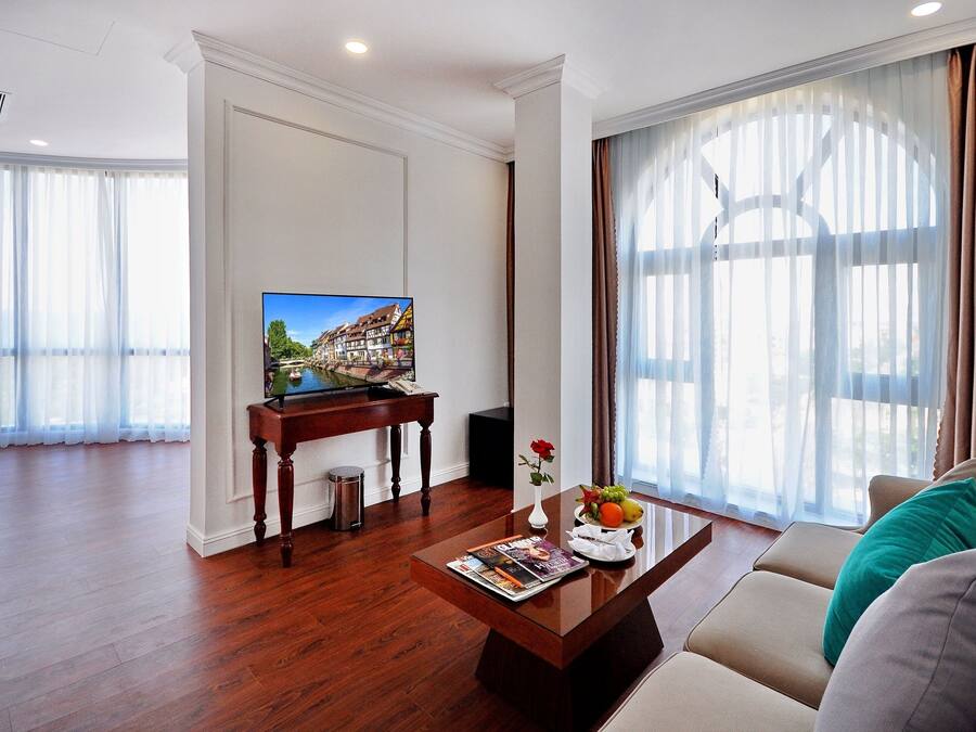 A modern living room with a wooden coffee table, a sofa, a TV, and a window with sheer curtains.