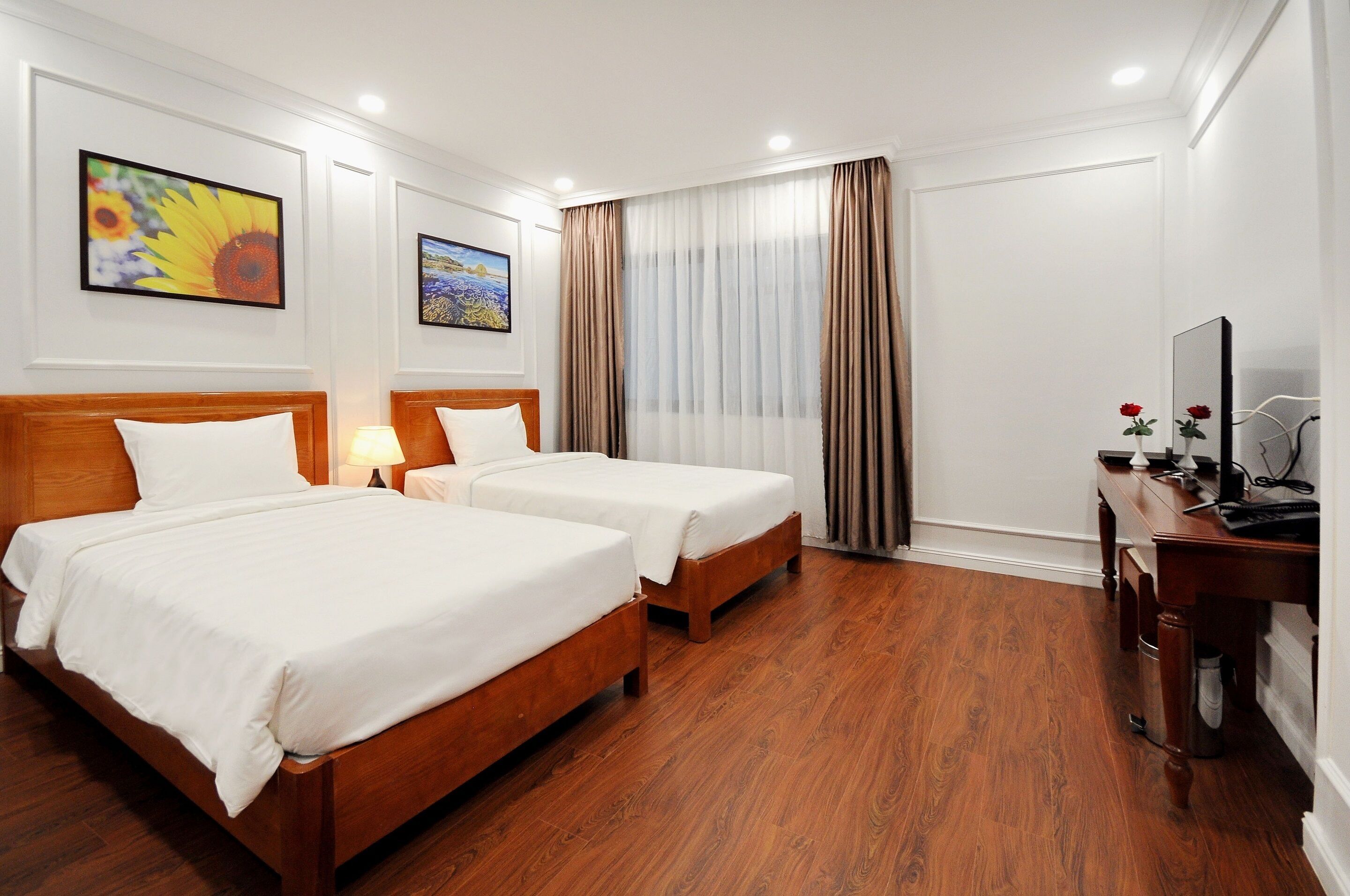 A hotel room with two wooden beds, a desk with a TV, and a large window with curtains.