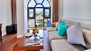 A living room with a large arched window, a beige sofa, a coffee table with magazines, and a small side table with a vase and flowers. - Sunflower Hotel (Tuy Hoa)
