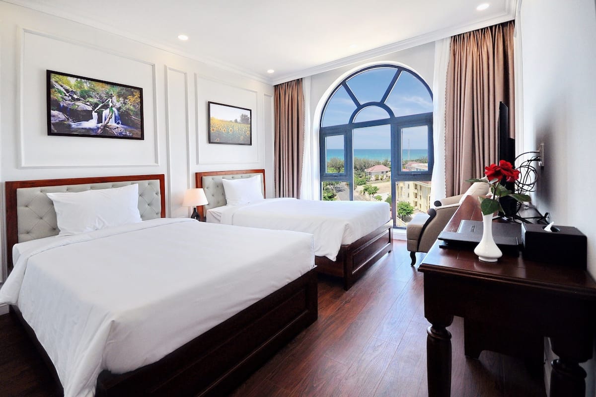 A hotel room with two beds, a desk, a chair, and a large window with a view.
