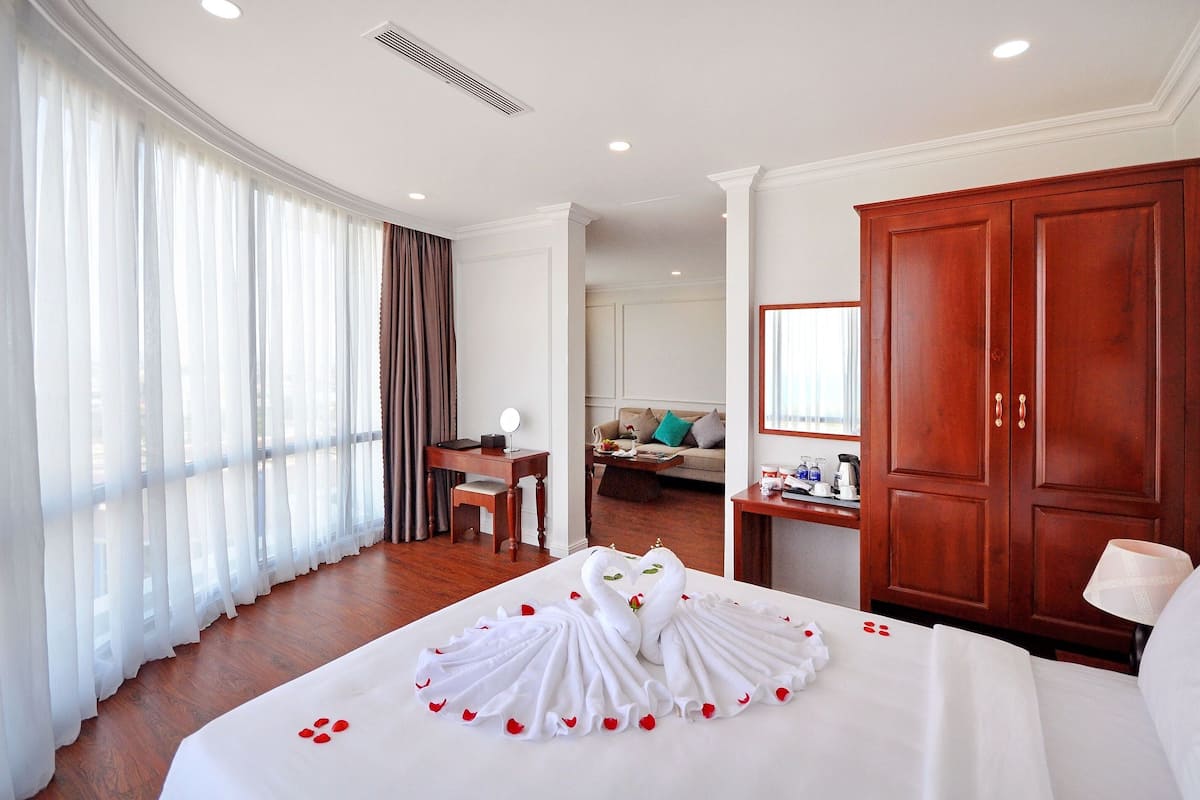 A hotel room with a bed, a desk, a wardrobe, and a view of another room.