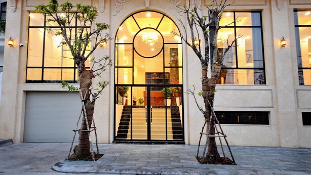 A building with a large arched entrance, a staircase leading inside, and two trees planted in front. - Sunflower Hotel (Tuy Hoa)