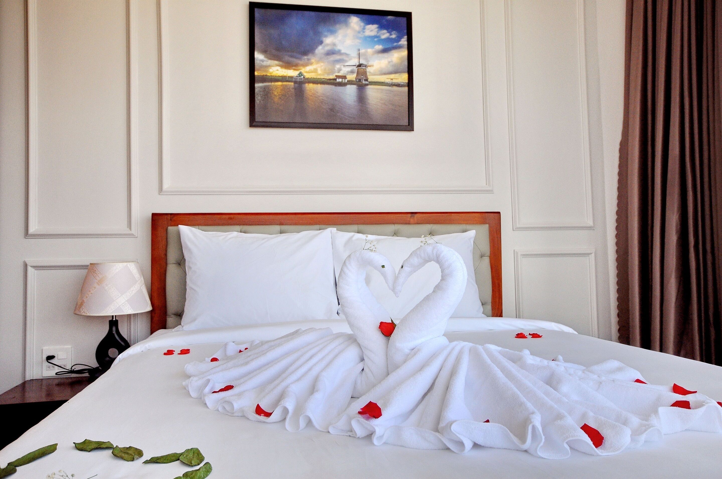 Una habitación de hotel con una cama, adornada con una toalla dispuesta en forma de corazón y un cuadro sobre ella.
