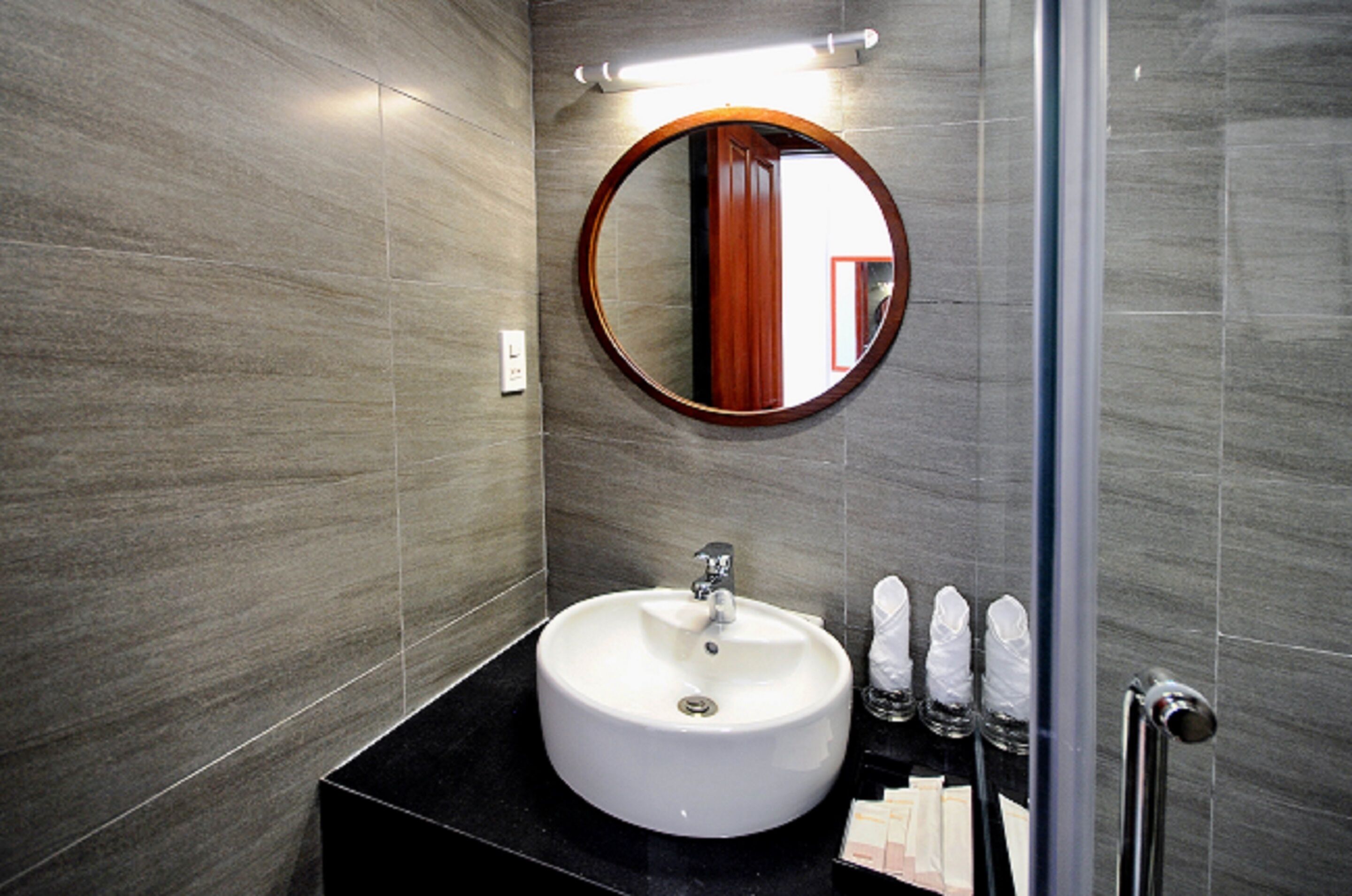 A modern bathroom with a round mirror, a white sink, and a black countertop.