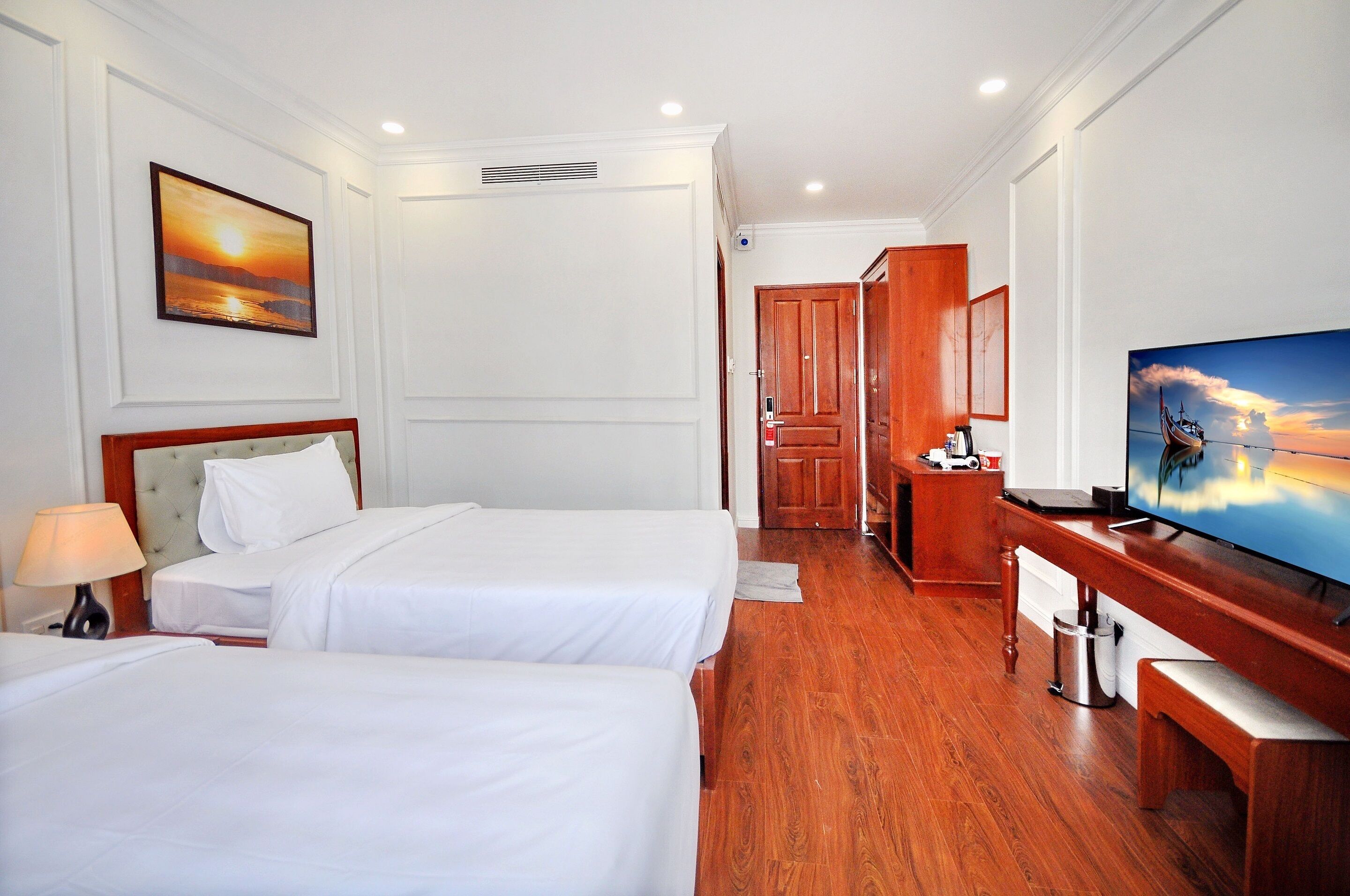 A hotel room with two beds, a TV, wooden furniture, and a painting on the wall.