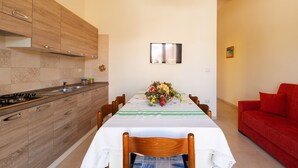 Une cuisine moderne avec des meubles en bois, une table à manger agrémentée d’un centre de table floral et un canapé rouge dans une pièce lumineuse.