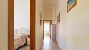 Un couloir avec un lit sur le côté gauche, une porte au fond et un tableau encadré au mur.