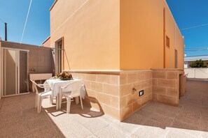 A patio area with a table and chairs, a small table with a vase, and a beige wall with a window. - 2033 Villetta Josè (Alliste)