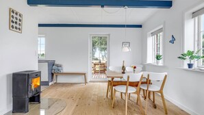 A modern kitchen with a wood-burning stove, a dining area with white chairs, and a view through a glass door to an outdoor patio. - 2 bedroom gorgeous home in Svaneke (Svaneke)