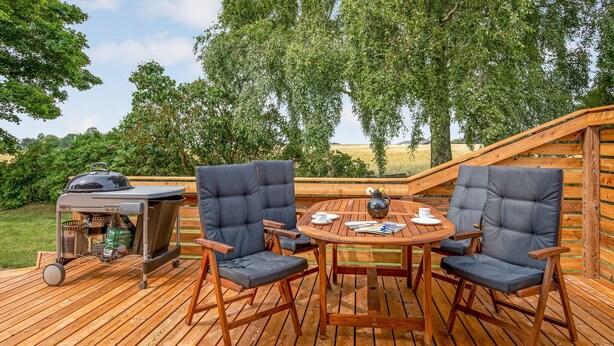 A wooden deck with a round table and four chairs, a grill, and a wooden pergola structure. - 2 bedroom gorgeous home in Svaneke (Svaneke)